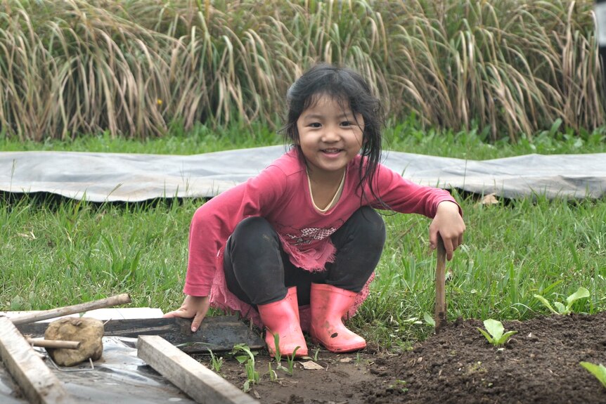 Young girl sits next to crop wearing a pink ballerina skirt and pink gumboots, smiling. 