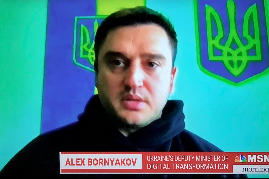 A blurry shot of a man facing the camera with ukraine flags in the background