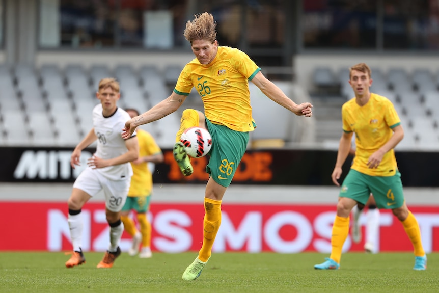 A soccer player wearing yellow and green kicks a ball