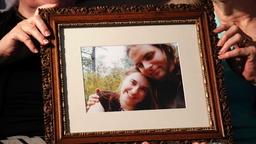 Hands holding a frame with a photo inside of a man and woman smiling and embracing.
