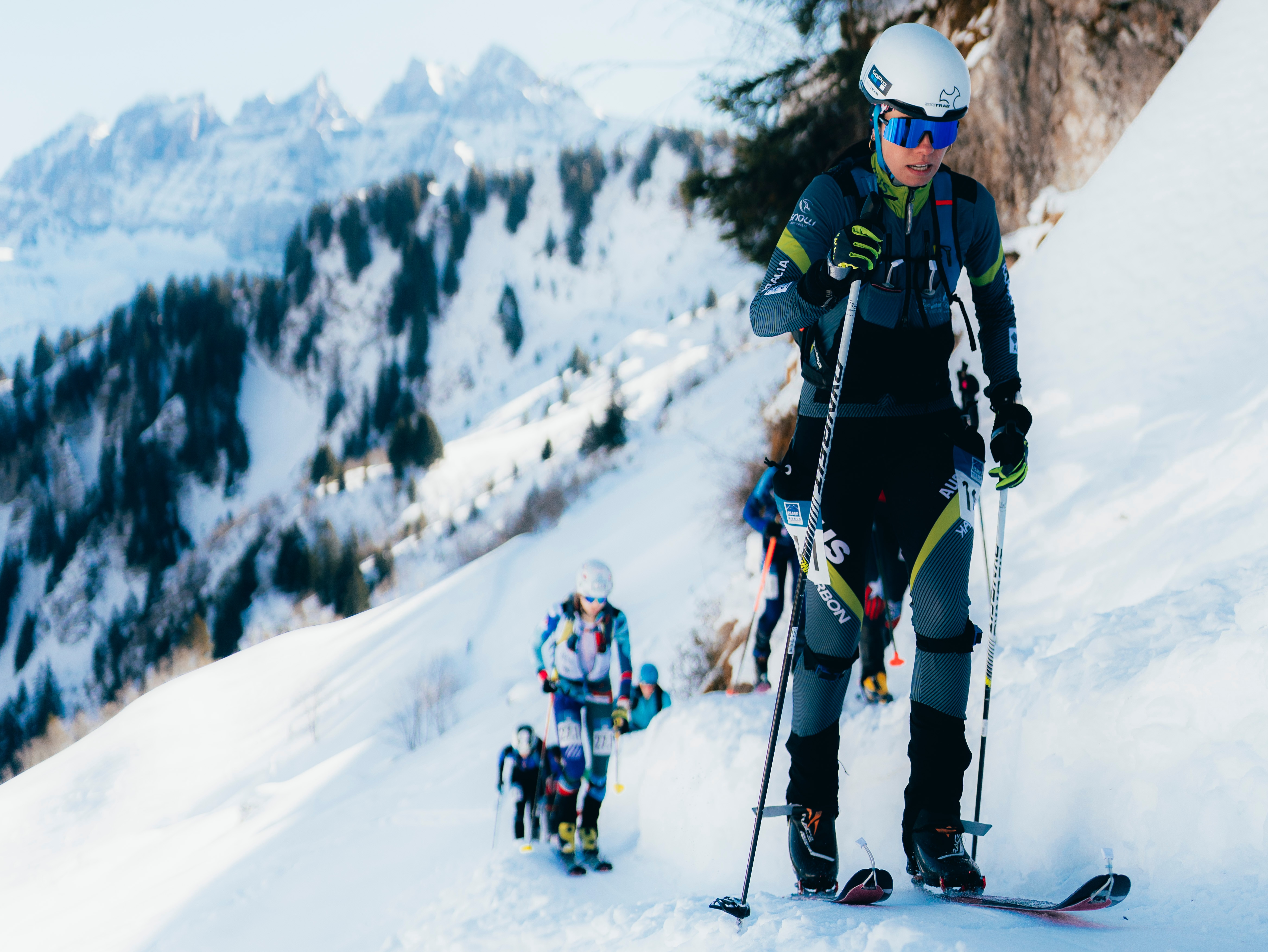 Uma atleta de alpinismo de esqui sobe uma montanha com esquis e usa bastões para ajudá-la