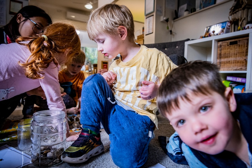 A childcare educator sitting on a mat, playing with kids