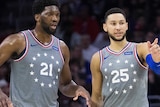 Ben Simmons and Joel Embiid converse on the court. Simmons points to something.