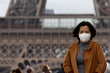 A woman wears a protective face mask in front of the Eiffel Tower.