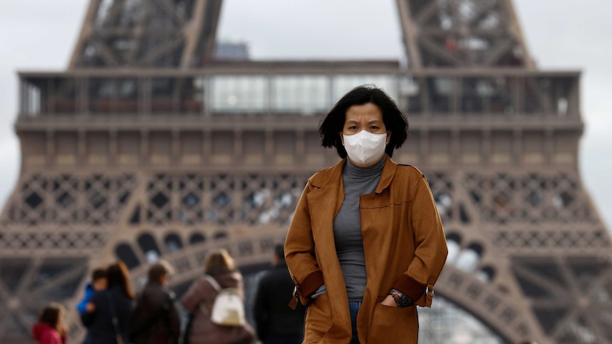 A woman wearing a protective face mask in front of the Eiffel Tower.