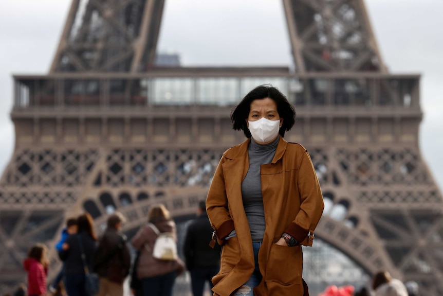 A woman wears a protective face mask in front of the Eiffel Tower.