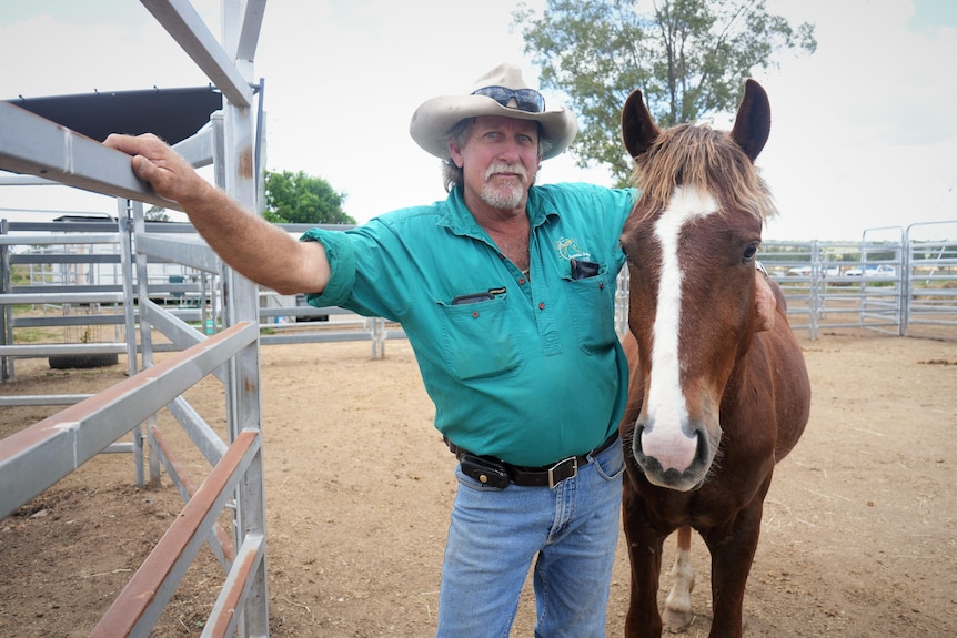 A man stands in yards with his arm slung over a horse. 