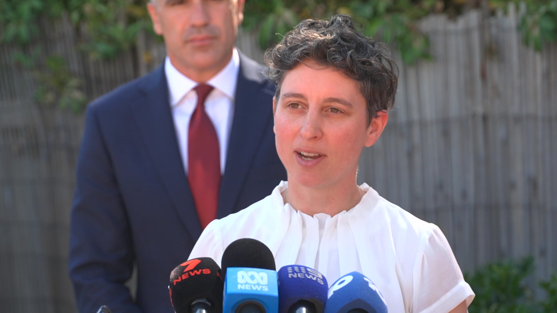 Kate Martin fica atrás de uma fileira de microfones de notícias enquanto fala.