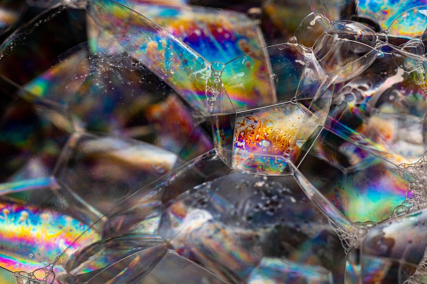 A tightly packed collection of hexagon-shaped, rainbow-coloured bubbles against a dark background.
