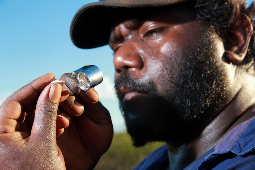 A  man looks at a lizard through a lens.