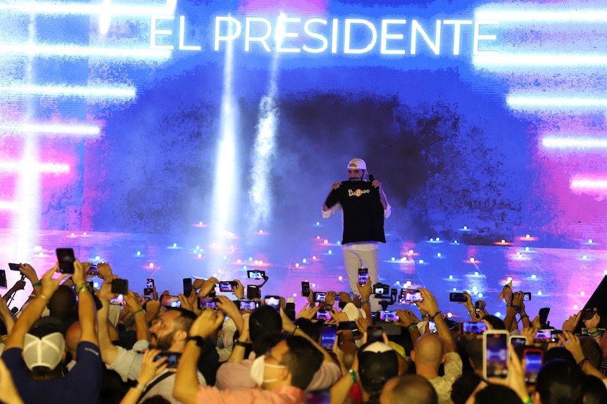 Nayib Bukele on stage with neon lighting behind him.  