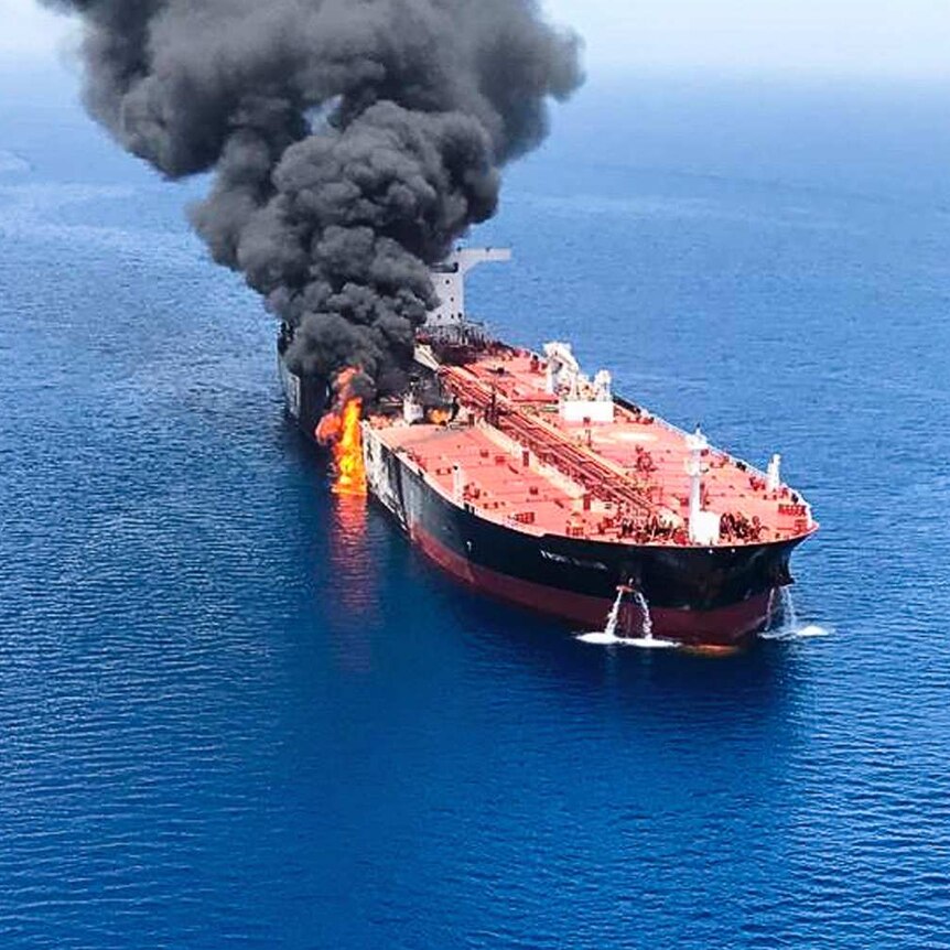 An aerial view of an oil tanker with flames and black smoke coming from one side.