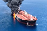 An aerial view of an oil tanker with flames and black smoke coming from one side.