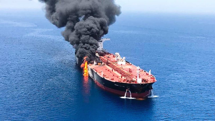 An aerial view of an oil tanker with flames and black smoke coming from one side.