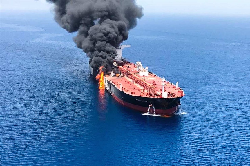 An aerial view of an oil tanker with flames and black smoke coming from one side.