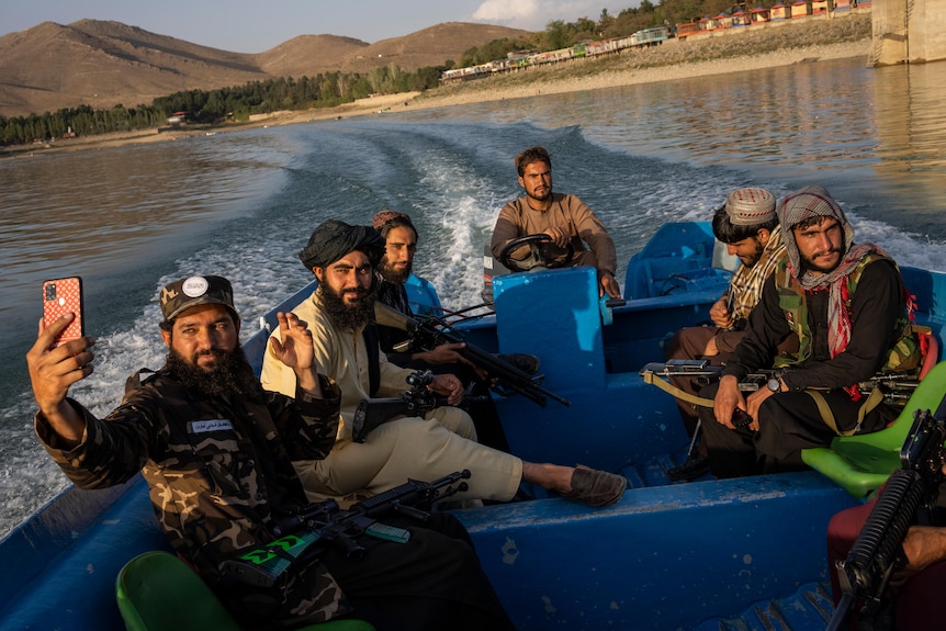 Taliban fighters take a selfie from the back of a boat sailing through a dam