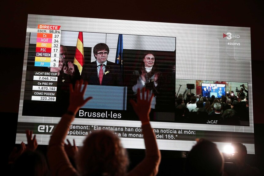 People watch as Carles Puigdemont speaks from Brussels on a giant screen in Barcelona.