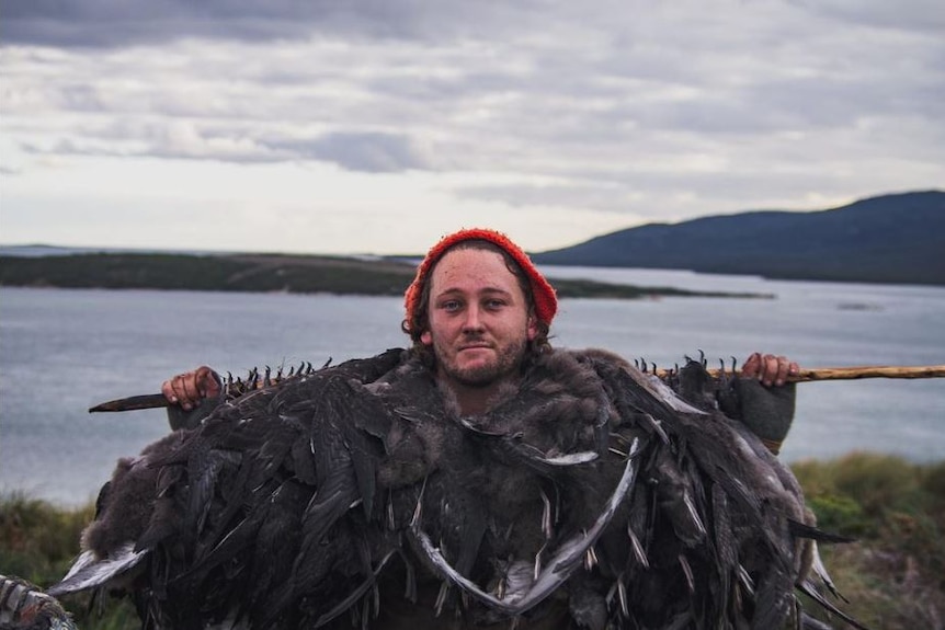 A man poses holding a spear over his shoulders from which hangs several dead birds.