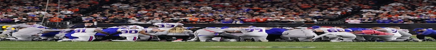 在队友受伤后的一场比赛中，一群布法罗比尔队的 NFL 球员跪在球场上围成一圈，低着头。