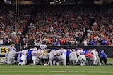 A group of Buffalo Bills NFL players kneel in a circle on the field with heads down during a game after a teammate's injury.