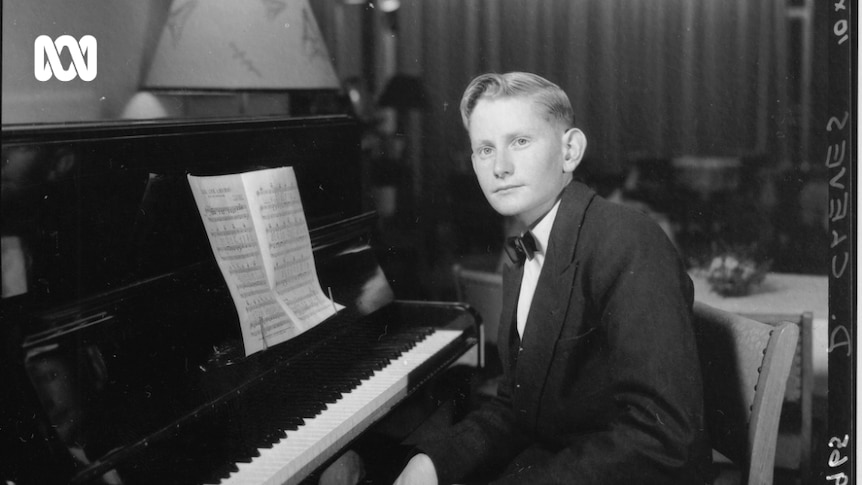 A black and white photo of a young man in a suit sitting at a black piano
