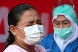 A woman wearing a mask cringes as she receives a vaccination from a healthcare worker