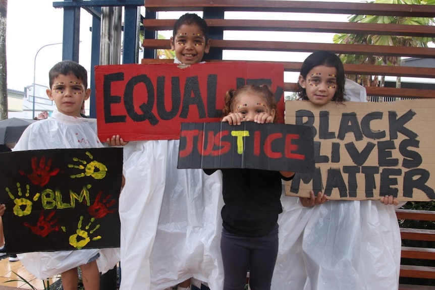 Four children, dressed in white raincoats, bear Black Lives Matter protest signs in Innisfail.
