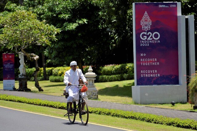 A man riding a bicycle passing G20 screen.