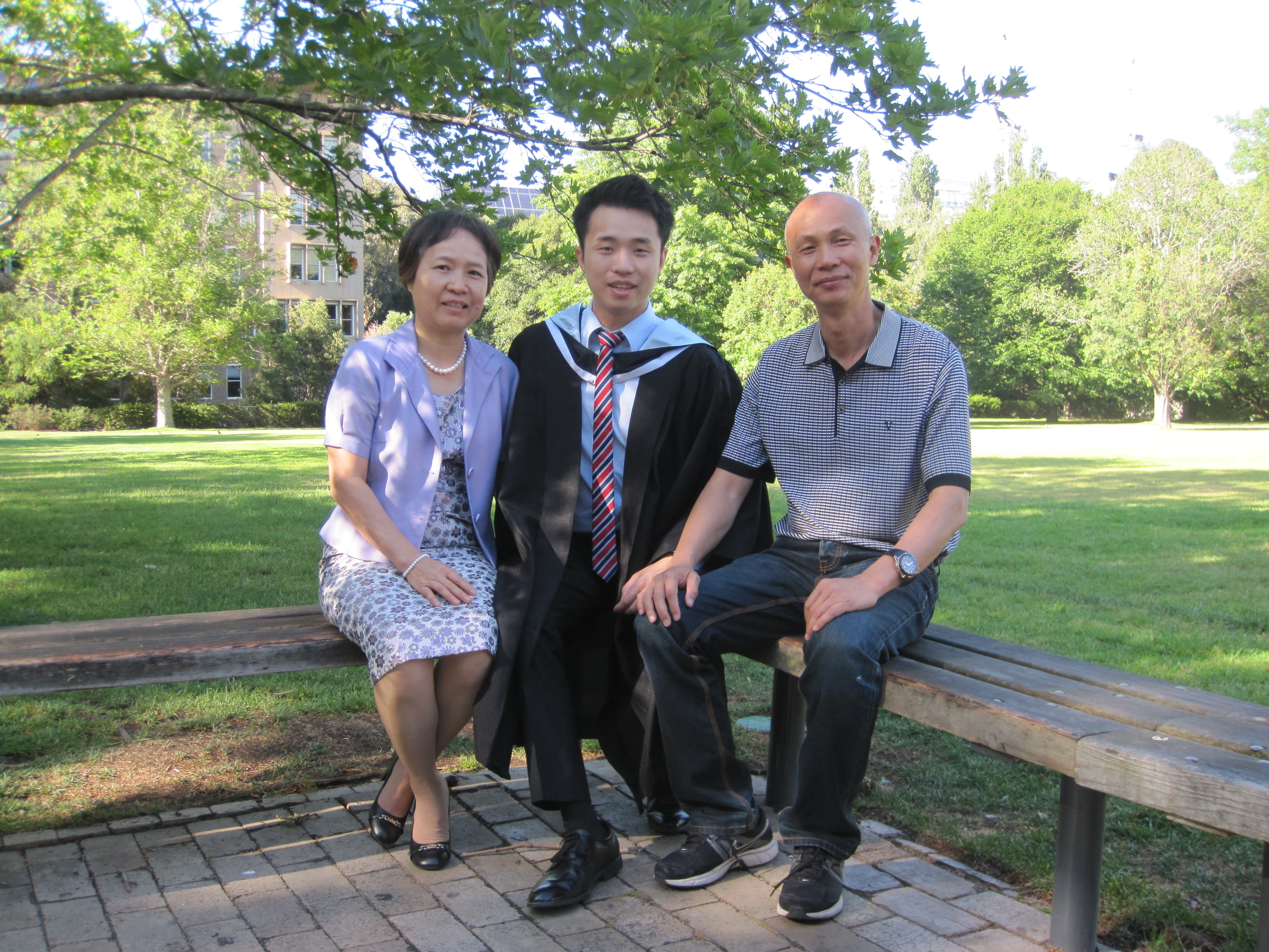 A young man in graduation robes sits with his parents