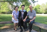A young man in graduation robes sits with his parents