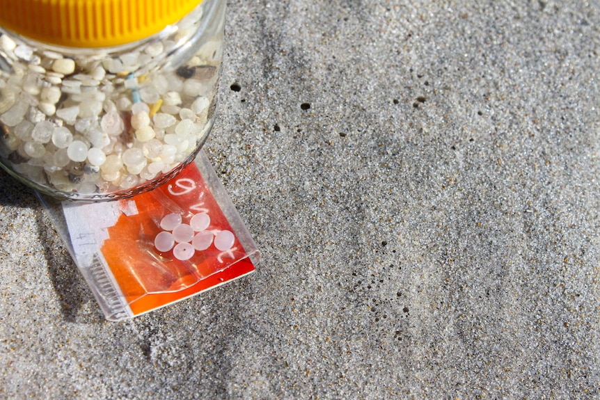 A sample of Durban nurdles - flat and opaque pellets in a plastic sleeve on the sand.