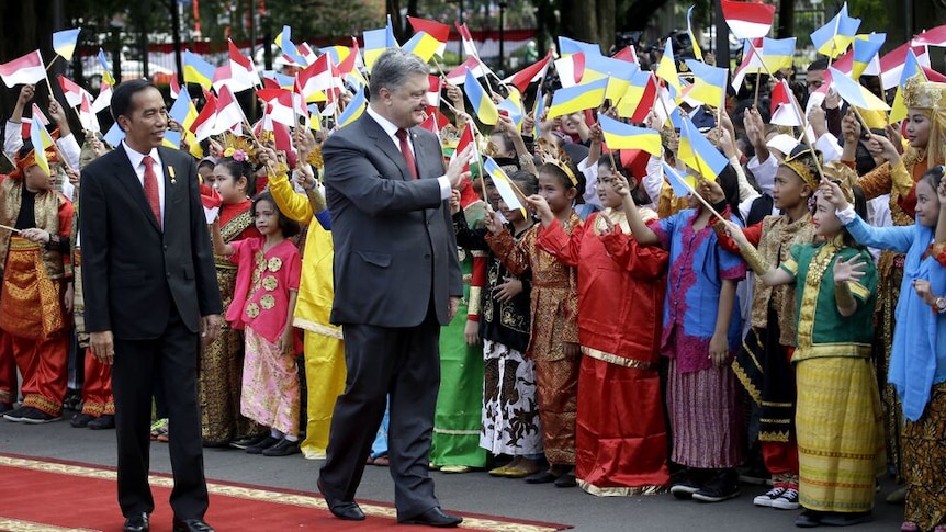 Two men in black coats were greeted by dozens of children in traditional clothes waving red-white and blue-yellow flags.