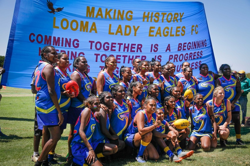 A team of female AFL players grouped together in front of a banner.