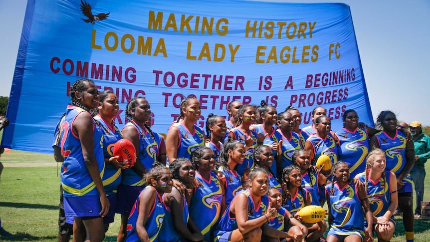 A team of female AFL players grouped together in front of a banner.