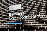 Metal lettering spells out Bathurst Correctional Centre on a black brick and white mortar wall