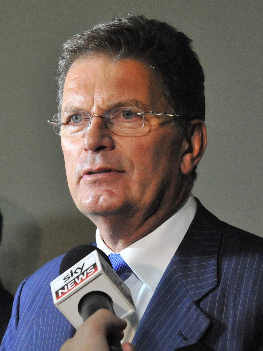Ted Baillieu stands in front of a microphone dressed in a blue suit as he speaks to reporters.