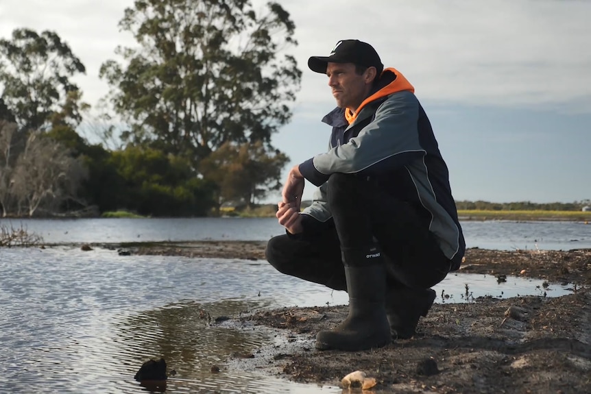 Farmer Jeremy Walker kneeling over flooded crops