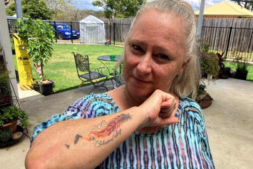 A middle-aged woman shows her forearm tattoo of a blazing feather.