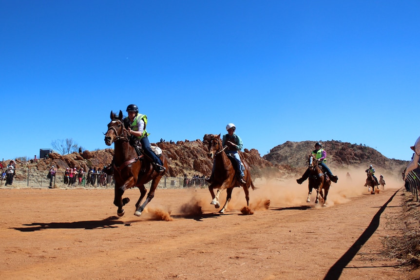 Jockeys ride down a dusty racetrack aboard horses.