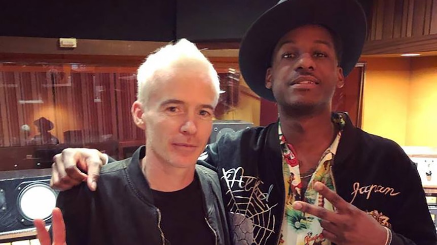 Leon Bridges and Robbie Chater of The Avalanches stand arm-in-arm in a studio giving peace signs