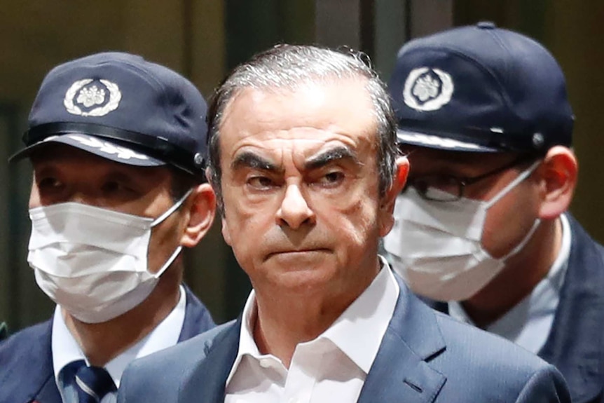 A close up of Carlos Ghosn with two men wearing masks