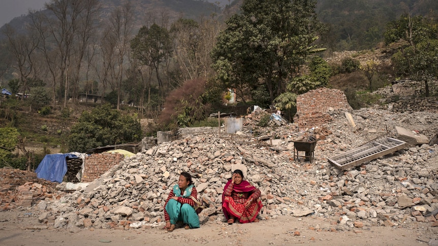 Nepal women sit by destroyed homes