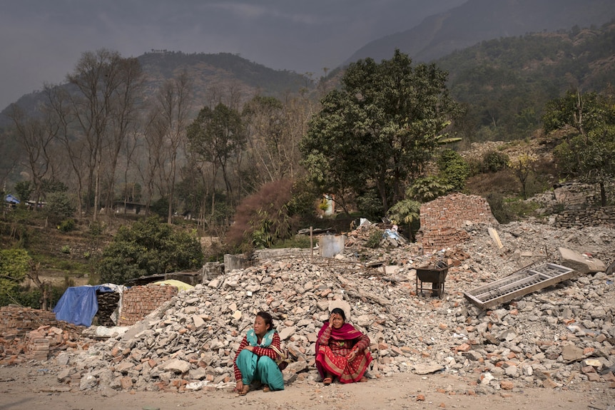 Nepal women sit by destroyed homes