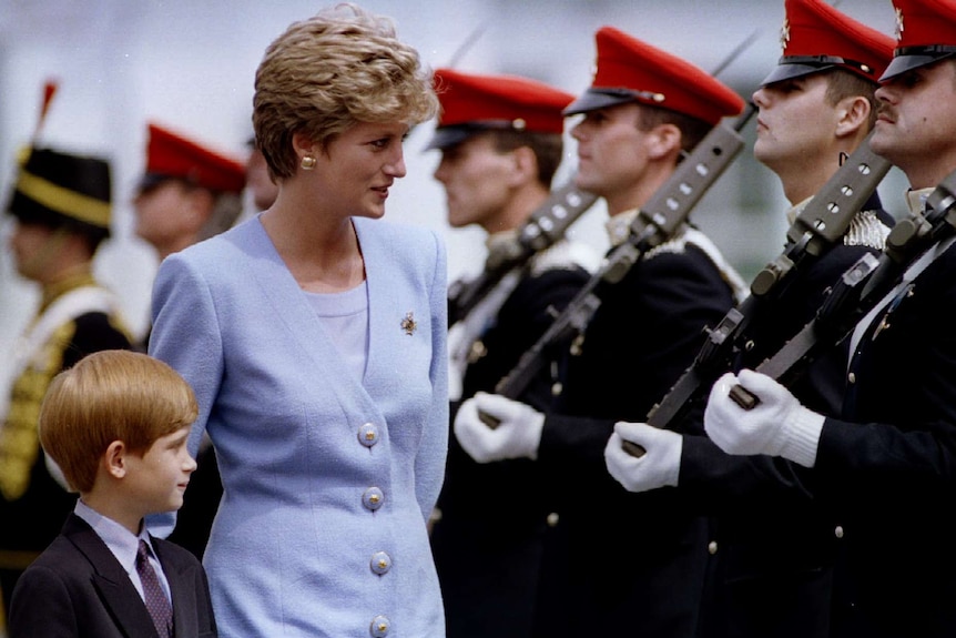You view Princess Diana in a tailored, lavender blazer and matching top, walking alongside troops in red hats with Prince Harry.