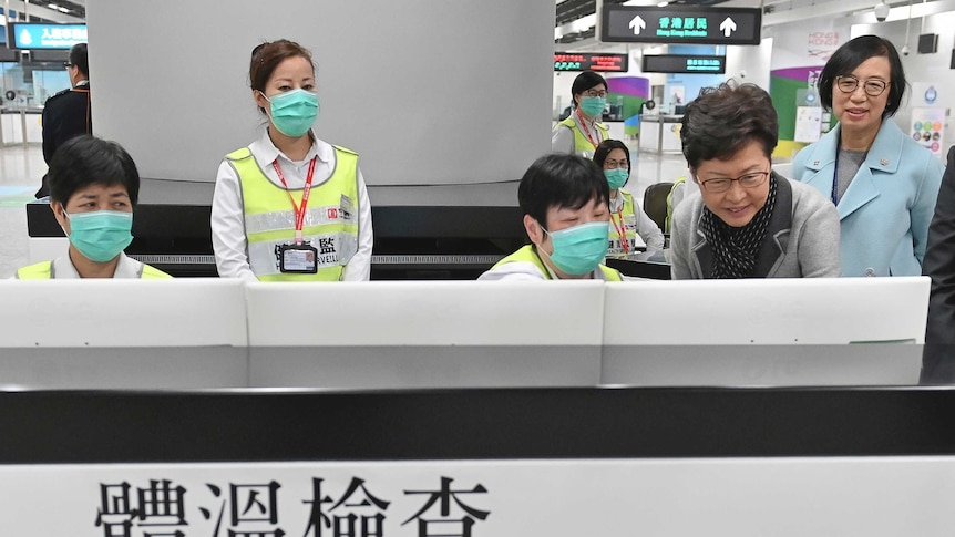 people stand behind a screen signed Temperature Check with face masks at an airport