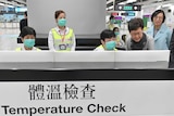 people stand behind a screen signed Temperature Check with face masks at an airport