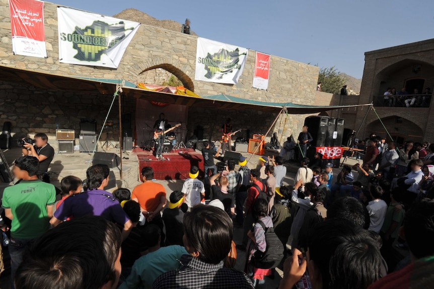 People gather around an outdoor stage, where a band performs