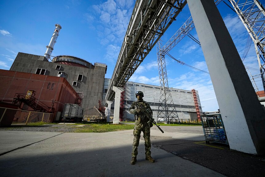 A Russian guard in military uniform, holding a rifle, while standing in front of a large industrial building.  