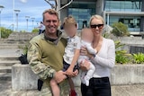 Danniel Lyon in an army uniform holding his son and his wife Caitland in a white jumper holding a baby