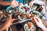 Bird's eye food of a group of people eating baked salmon, pita, and roast vegetables in a restaurant.